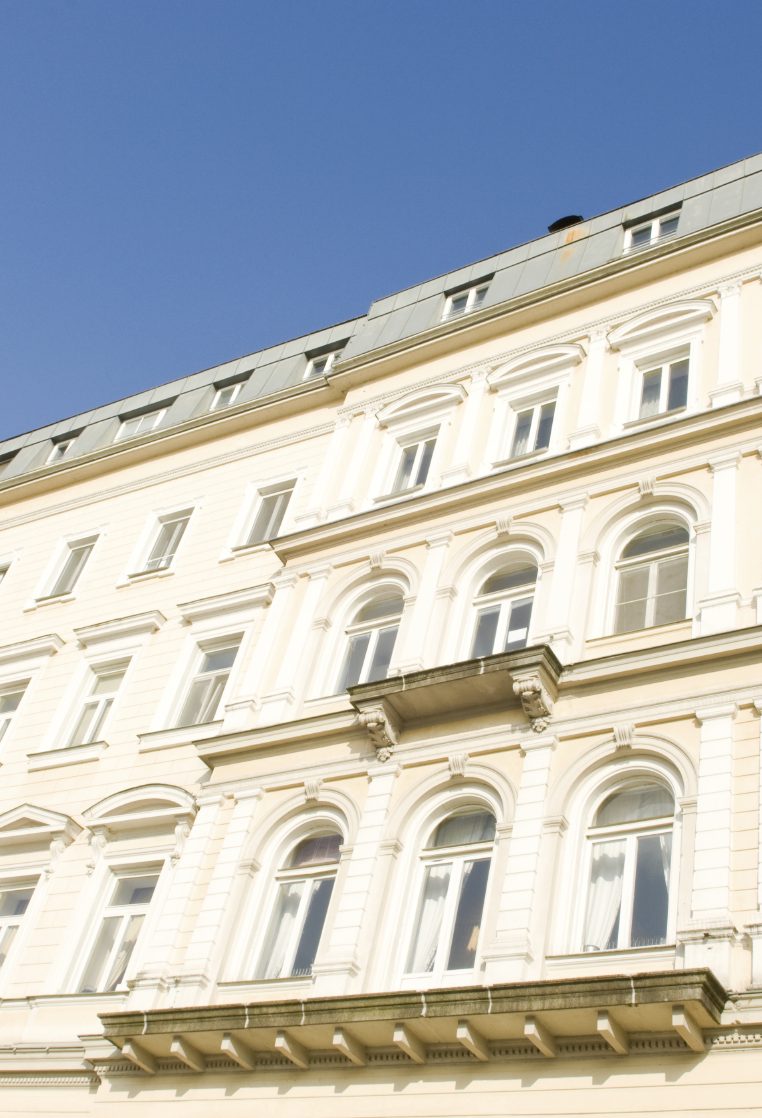 Helle Fassade mit Stuckelementen eines historischen Gebäudes unter blauem Himmel.