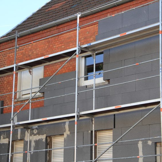 Fassade eines Hauses mit einem Gerüst und teilweise erneuertem Putz und Dämmung