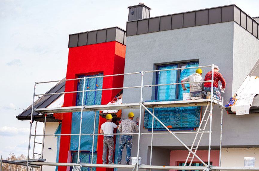 Arbeiter führen Renovierungsarbeiten an einer Fassade mit Gerüst durch.